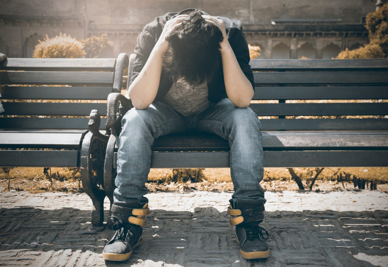 Man sitting on bench with head resting in his hands showing signs of depression or sadness.