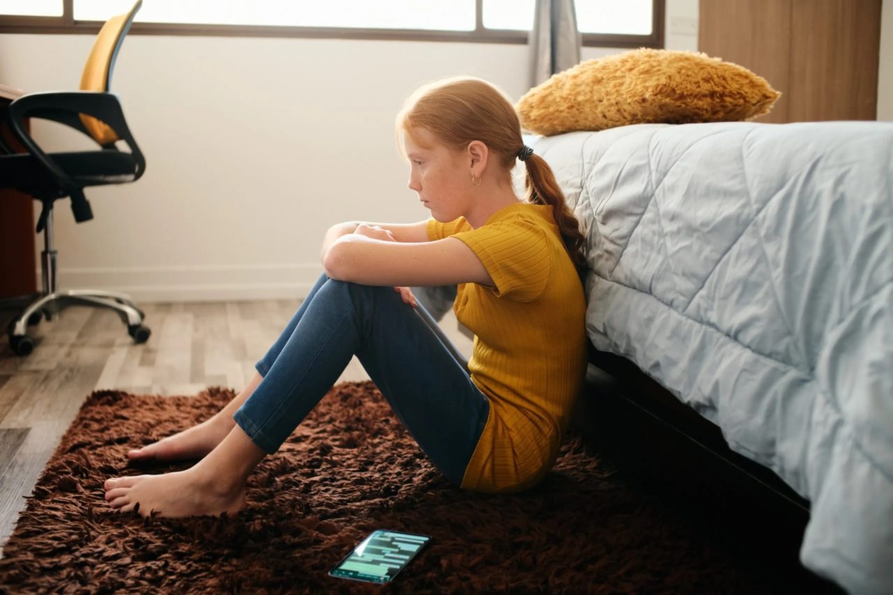Girl showing signs of distress sitting on the floor of her bedroom